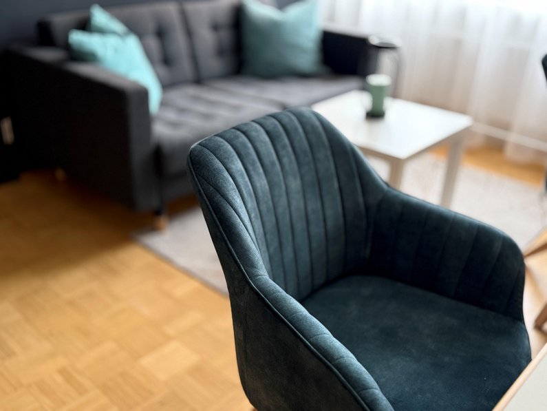 Künstlergarderobe, Detailfoto des Stuhls, Farbe petrol, Samt, weich gepolstert, im Hintergrund das Sofa mit Sofakissen, Wohnzimmergefüh
