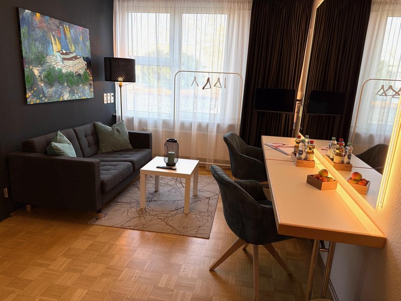 Künstlergarderobe, Sofa, Tisch, bequeme Stühle, Stehlampe, Bild an der Wand, Teppich unter dem Couchtisch, Wohnzimmergefühl